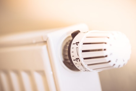 Ein weißer Heizkörper mit einem Thermostatventil, das auf die Einstellung 3 gedreht ist, strahlt Wärme in einem sanften Licht aus.