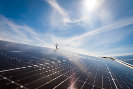 Ein glänzendes Solarpanel reflektiert Sonnenlicht unter einem klaren blauen Himmel, während die Sonne hell strahlt.