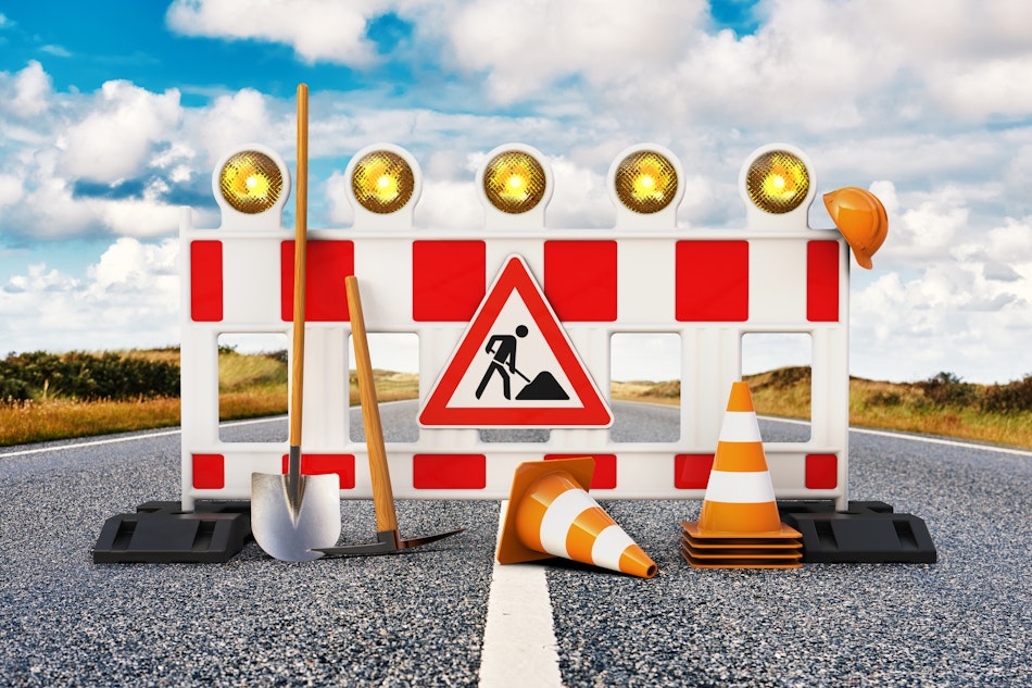 Straßenabsperrung in Rot-weiß mit Straßenkegeln, Spitzhacke und Schaufel für Baustelle