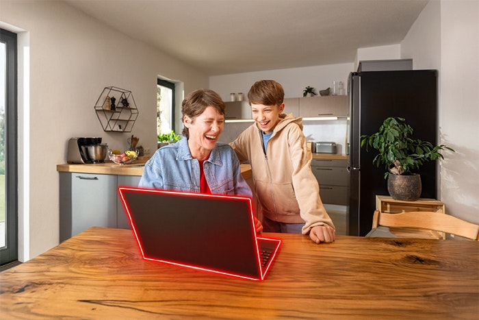 Eine lächelnde Frau und ein Junge betrachten gemeinsam einen beleuchteten Laptop auf einem Holztisch in einer modernen Küche.