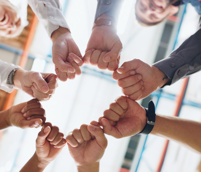 Mehrere Menschen bilden einen Kreis und strecken ihre Fäuste zur Mitte, symbolisieren Teamarbeit und Zusammenarbeit in einem modernen Büro.