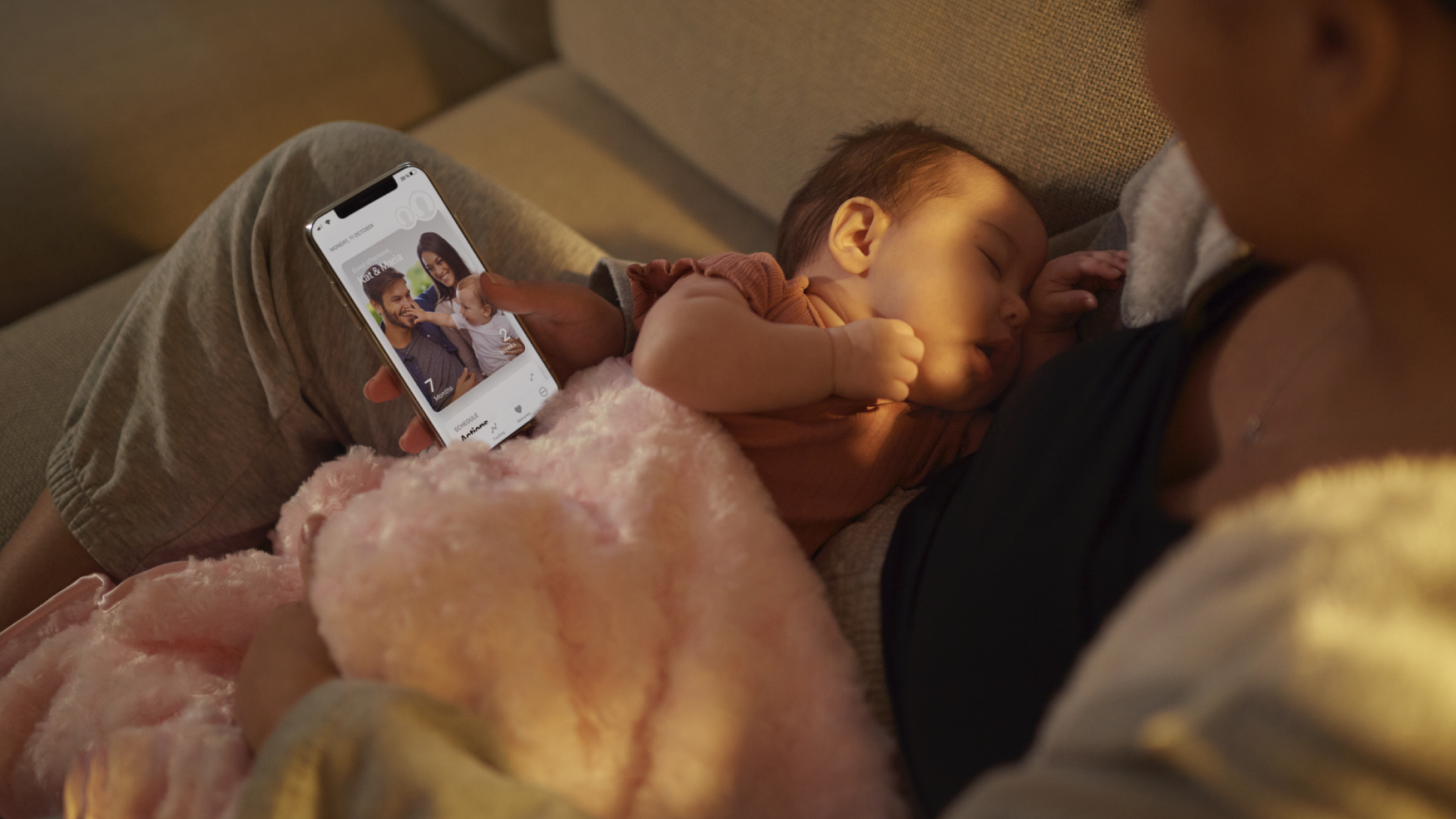 Sitting woman holding a sleeping baby and checking a baby app on her mobile