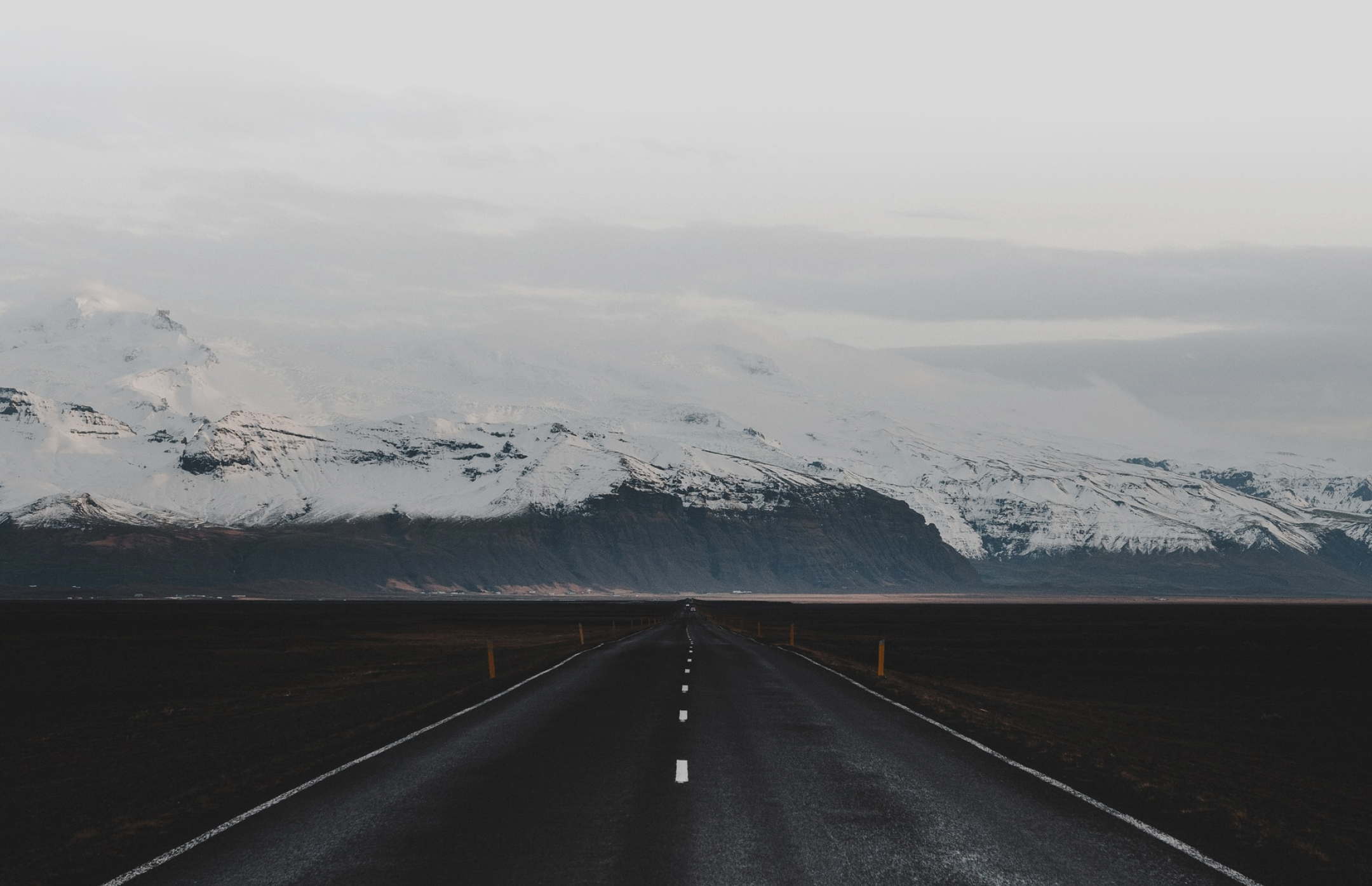 Image of a highway in the middle of nowhere with snowy montains at the horizon.