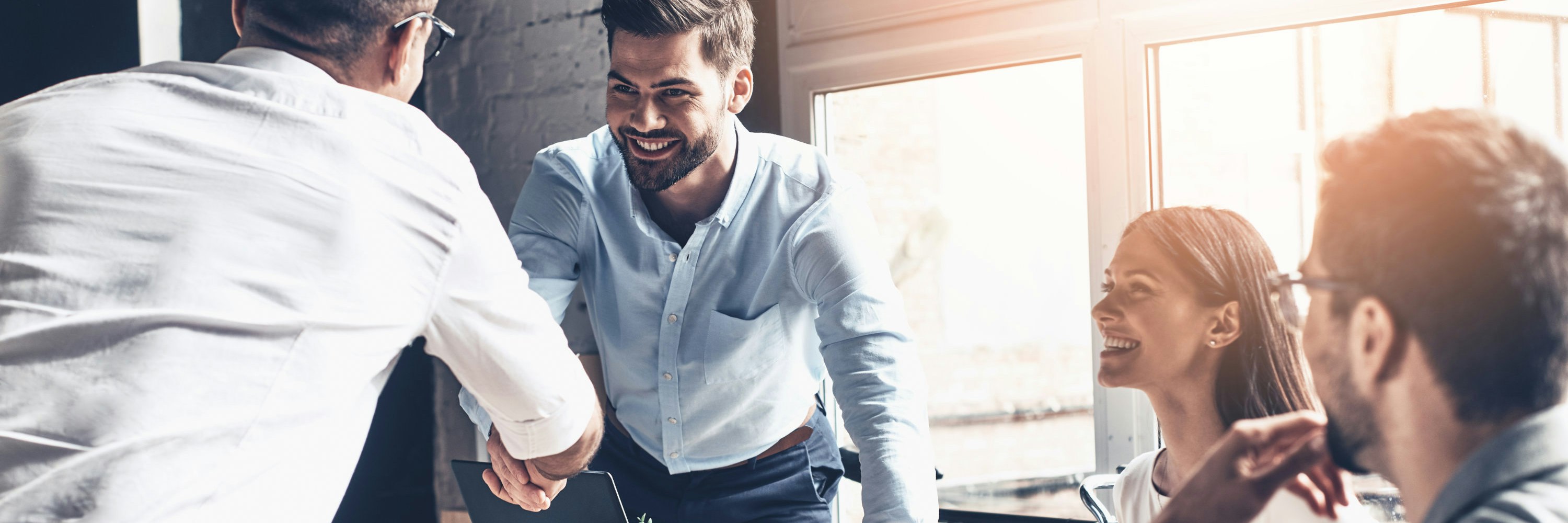 Young modern men in smart casual wear shaking hands and smiling while working in the creative office.