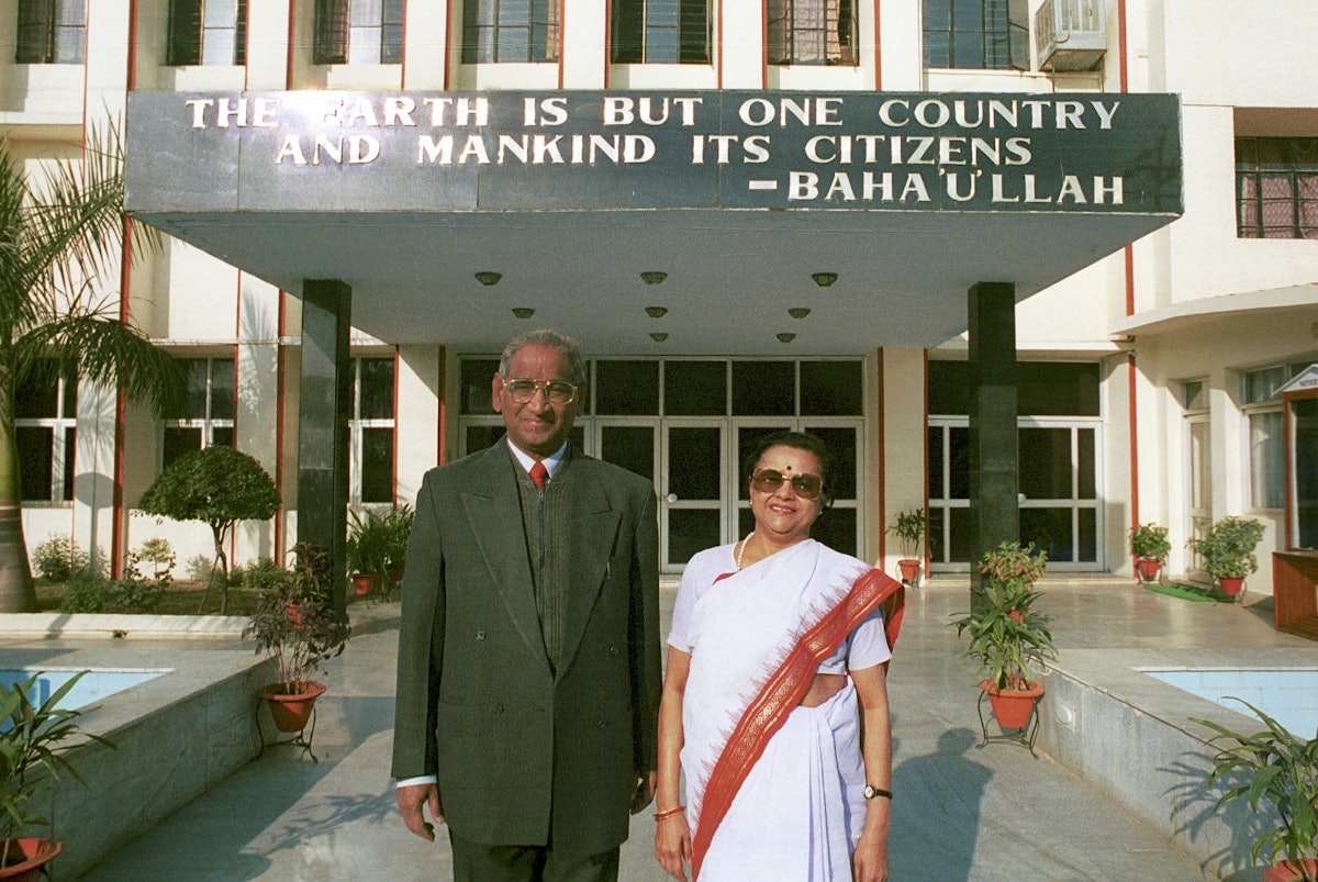 Jagdish Gandhi and Bharti Gandhi, founders of the City Montessori School in Lucknow, India.| They are standing in front of the main building of Gomti Nagar branch of the School, one of 20 branches in Lucknow. A quote from Bahá’u’lláh, "The earth is but one country and mankind its citizens" is on the awning behind them.