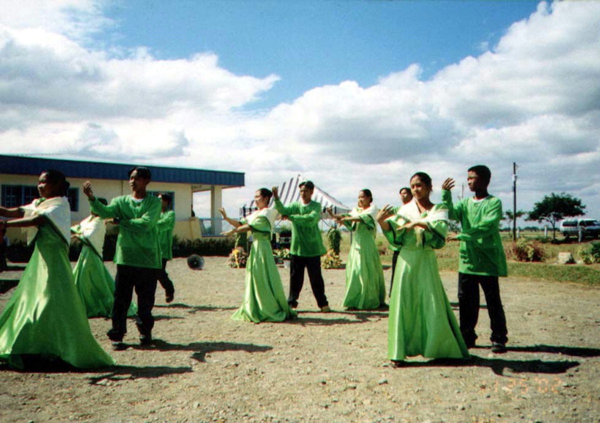 In a festive celebration, the Baha’i community of the Philippines officially inaugurated its new radio station on 26 November 2002. Shown here is a performance by the Tondod Public High School Dance Troupe.| The radio station building is in the background. It is the seventh Baha’i radio station in the world.