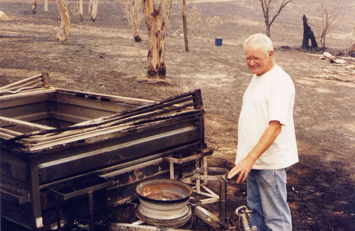 Caretaker John Burnett looking at his camper-trailer burnt in the blaze that threatened the Bahá'í Center in Canberra.