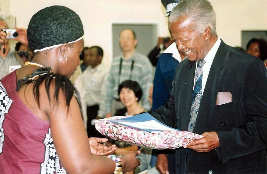 On behalf of the Baha'i community, Eva Mnisi presents a gift to A. K. Hlophe, the representative of the Queen Mother.