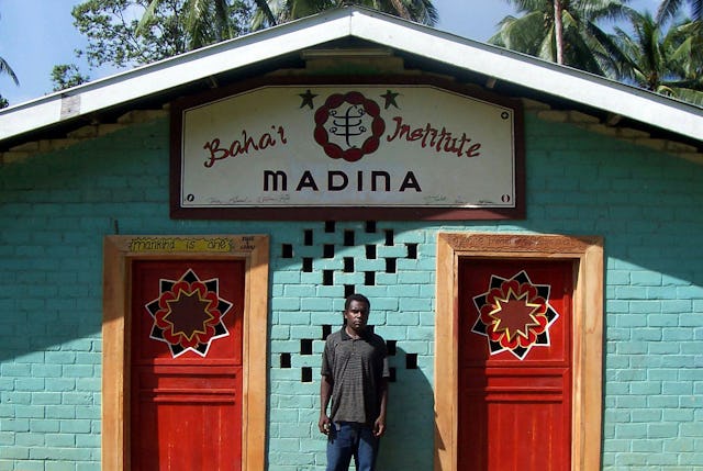 Madina Baha'i Rodney Kelep outside the local Baha'i institute. Inside, the ceiling is covered with nine pointed stars made from seashells, and each window's upper frame is carved with traditional motifs.