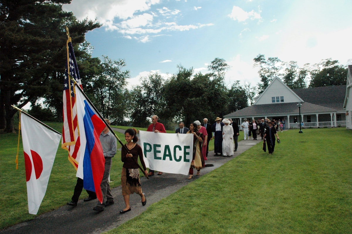 Participants in the 100th anniversary commemoration of the Portsmouth Peace Treaty march across the grounds at Green Acre Baha'i School carrying flags of the three nations that participated in the treaty signing 100 years ago, Japan, the United States, and Russia.