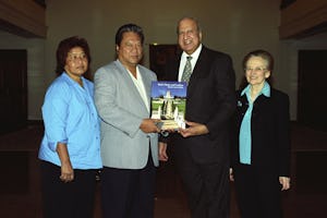 A member of the Universal House of Justice, Dr. Peter Khan, second from right, presenting President Kessai Note of the Marshall Islands with a book illustrating the Shrine of the Bab and its surrounding terraces. At left is Mrs. Mary Note and, at right, Dr. Janet Khan.