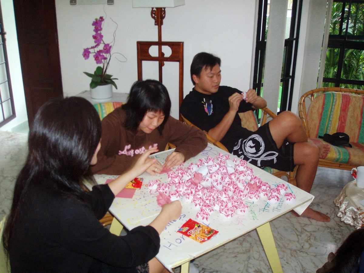 Project Million Lotus 2006 aims to have young people of all races and religions in Singapore make a million paper lotuses as symbols of purity and harmony. Shown, left to right, are Kuek Shao Zhen, Yuen Yi Ying, and Chong Ming Hwee, all Baha'is, folding paper flowers at the Singapore Baha'i Center on 15 April 2006.