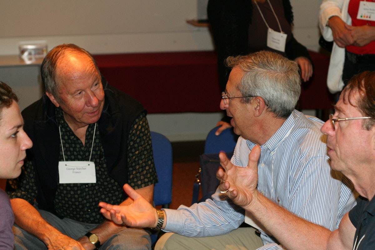 George Starcher (back left), EBBF co-founder, and Larry Miller (back right) actively engaged in conversation with each other, while Arthur Dahl (front right), an EBBF governing board member, explains a concept to Cornelia Raportaru of AIESEC International.
