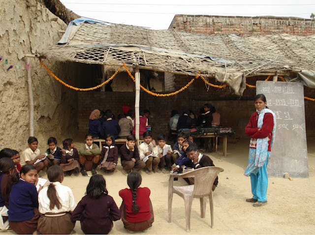 A mathematics class at New Ideal Academy in a village near Lucknow meets in the open air, while students in another class gather at a table under the shelter.