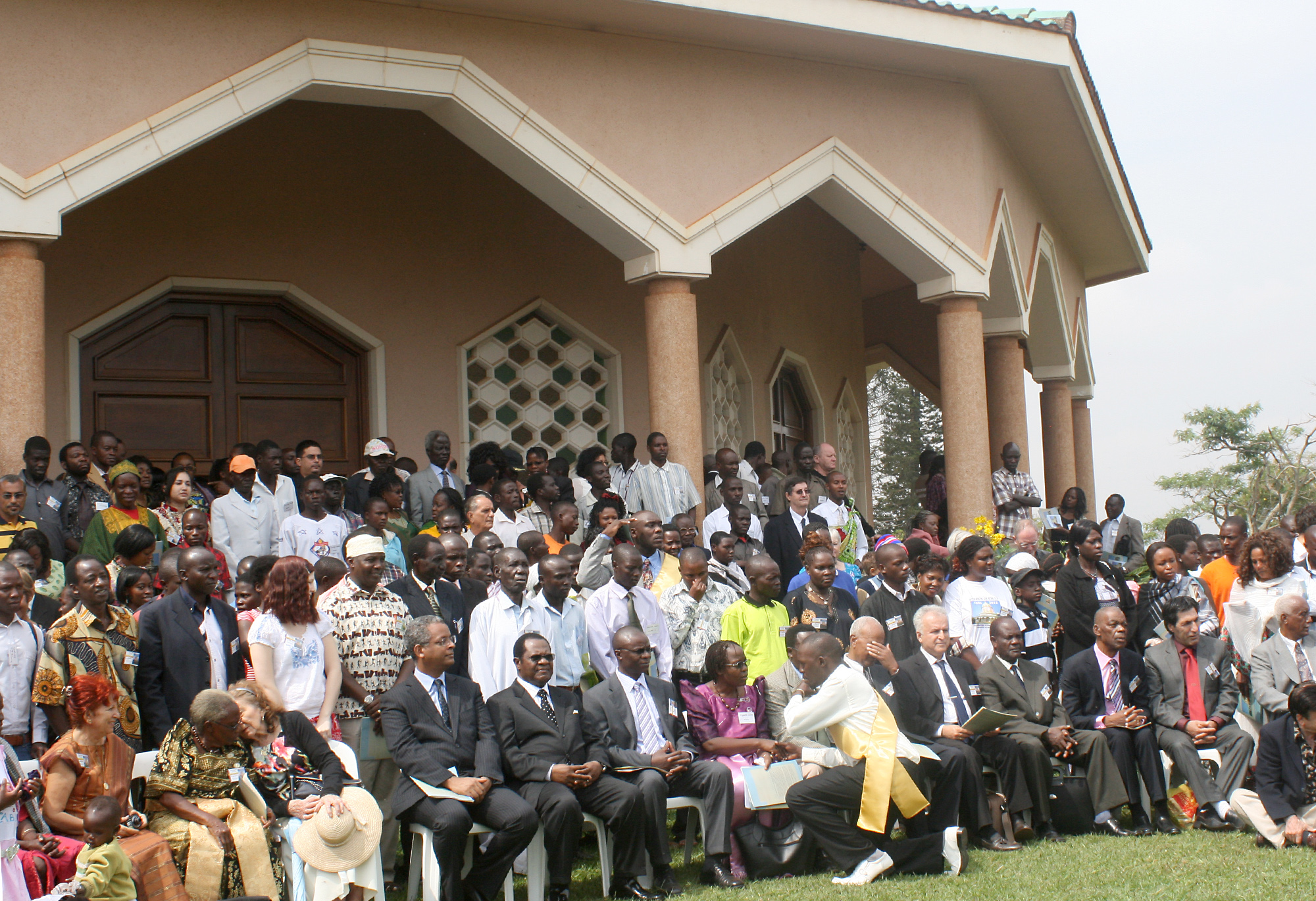 Guests assemble for a group photograph in front of the Baha'i House of Worship in Kampala, Uganda, on the occasion of its fiftieth anniversary. The Chief Justice of Uganda, the Honorable Mr. Justice Benjamin J. Odoki, is seen seated at the front, wearing dark glasses.