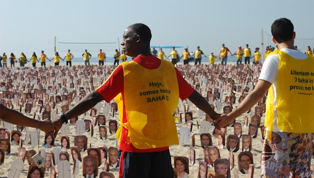 Campaigners join hands around almost 8,000 photographs of Iran's seven imprisoned Baha'i leaders at a rally calling for human rights in Iran, held at Rio's Copacabana Beach, 19 June 2011. Their yellow vests read, "Today we are all Baha'is" and "Free the 7 Baha'is imprisoned in Iran". Vests were also distributed to beach-side traders and passers-by who wished to identify themselves with the cause.