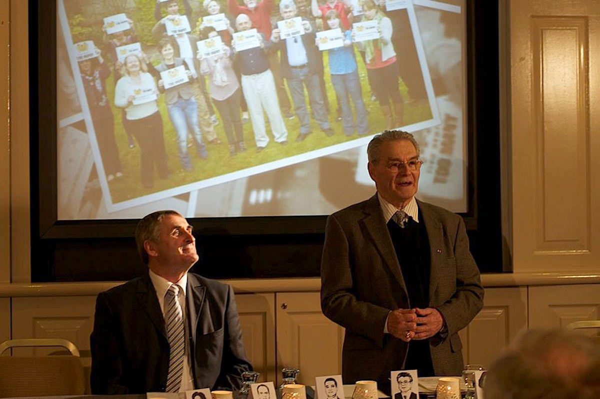 Tomi Reichental, at right, standing, speaks at the Five Years Too Many event in Ireland on 15 May. On the left is Brendan McNamara of the Irish Baha'i community.