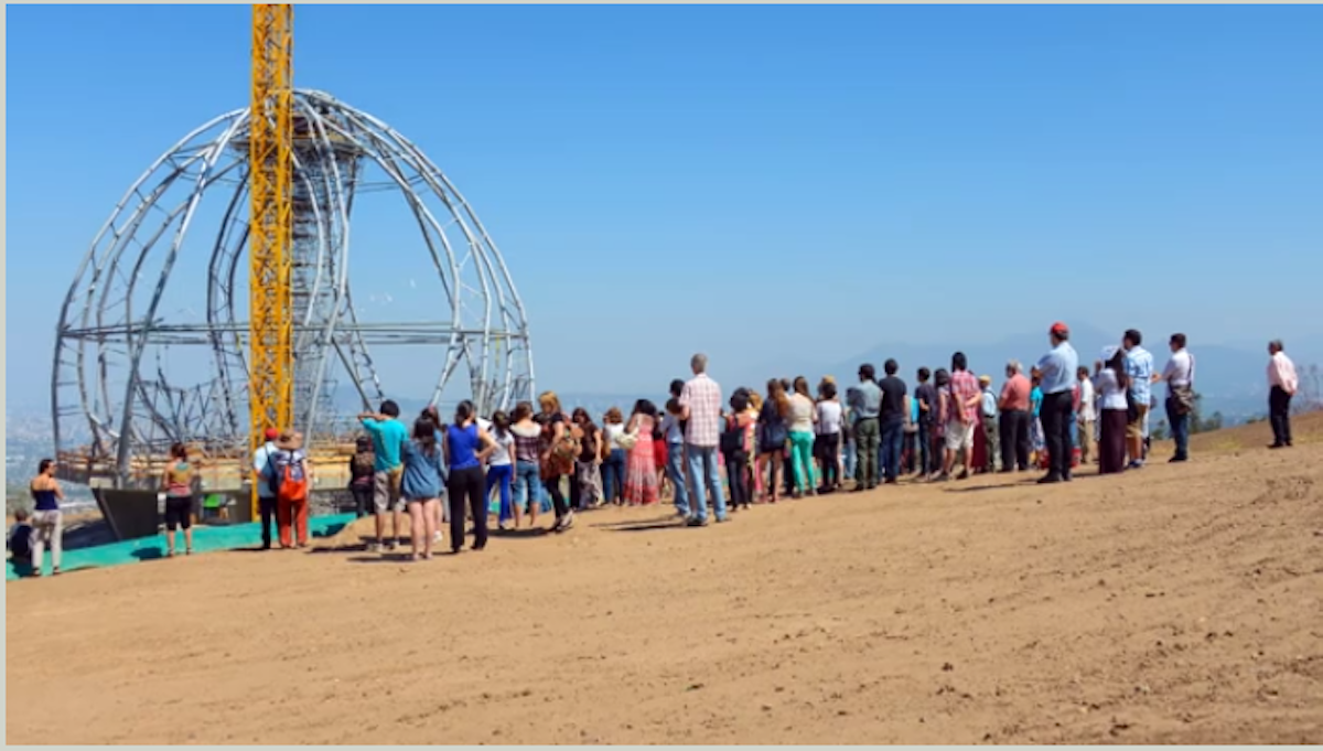 Community members gather at the site of the House of Worship, with the superstructure in the background.
