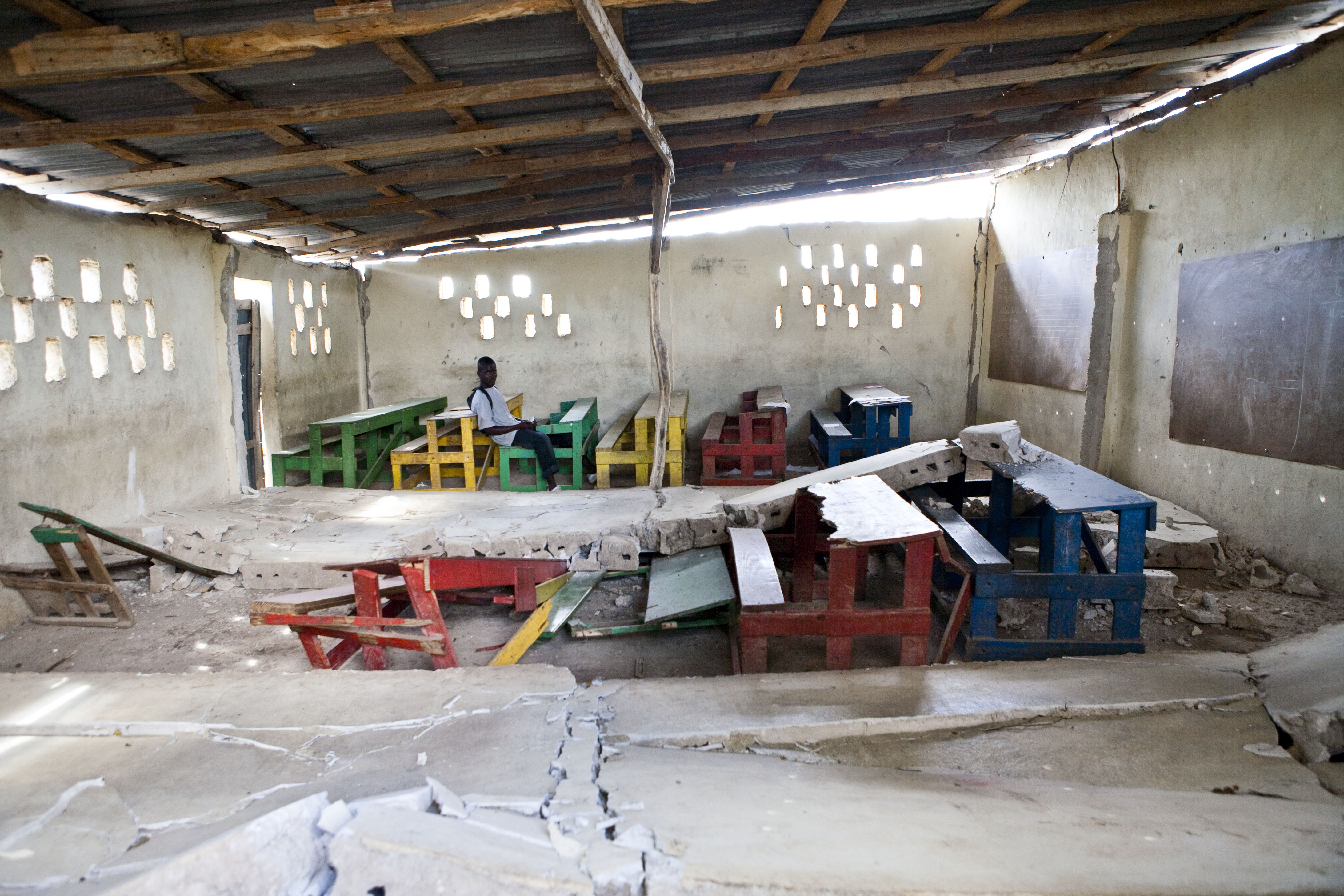 Nearly three weeks after the earthquake, a lone youth sits in a school that was severely damaged. The vastness of the destruction and the collapse of infrastructure hamper the clean-up efforts.