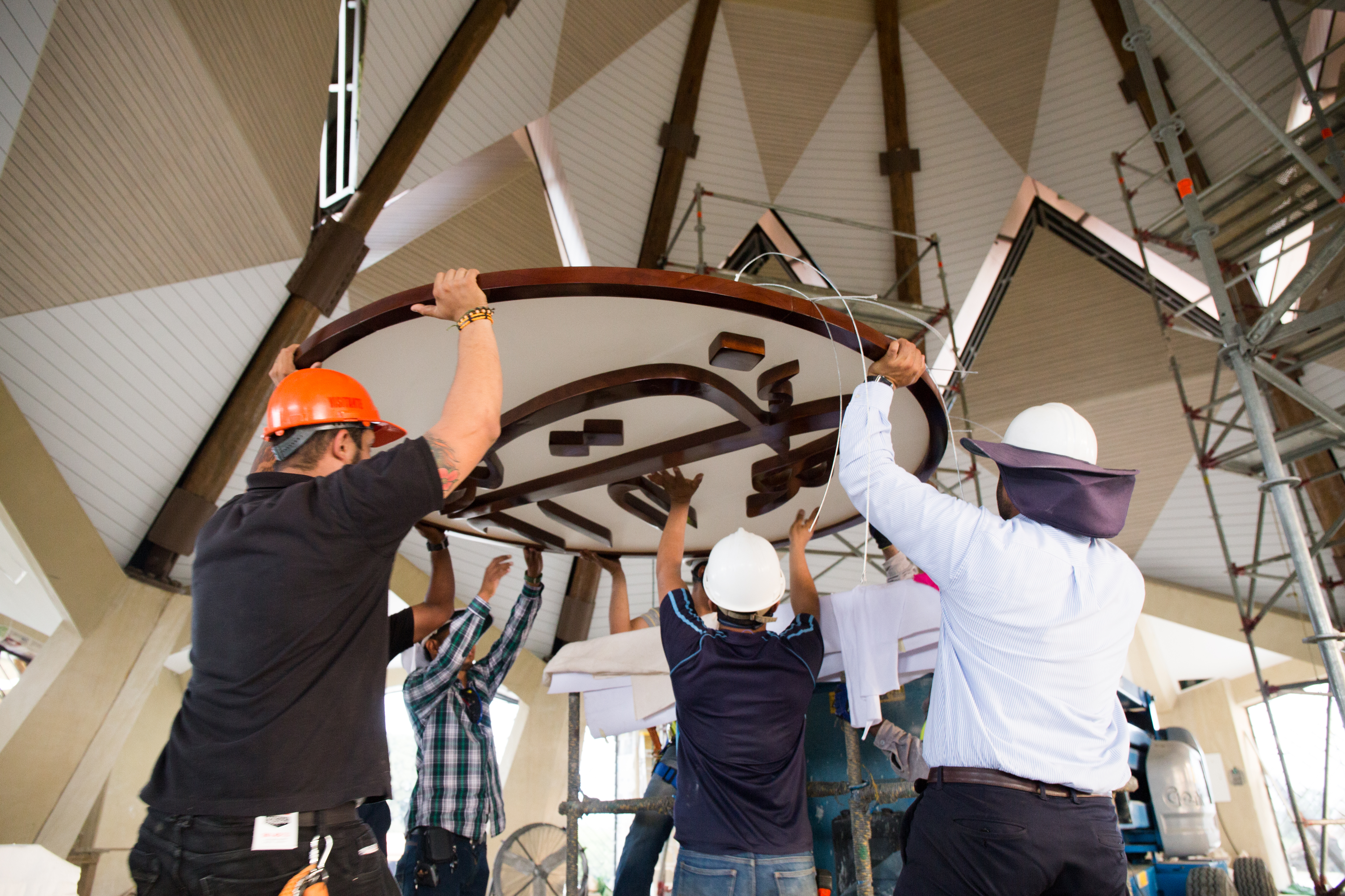Workers raise the Greatest Name symbol before installing it at the apex of the Temple’s dome.
