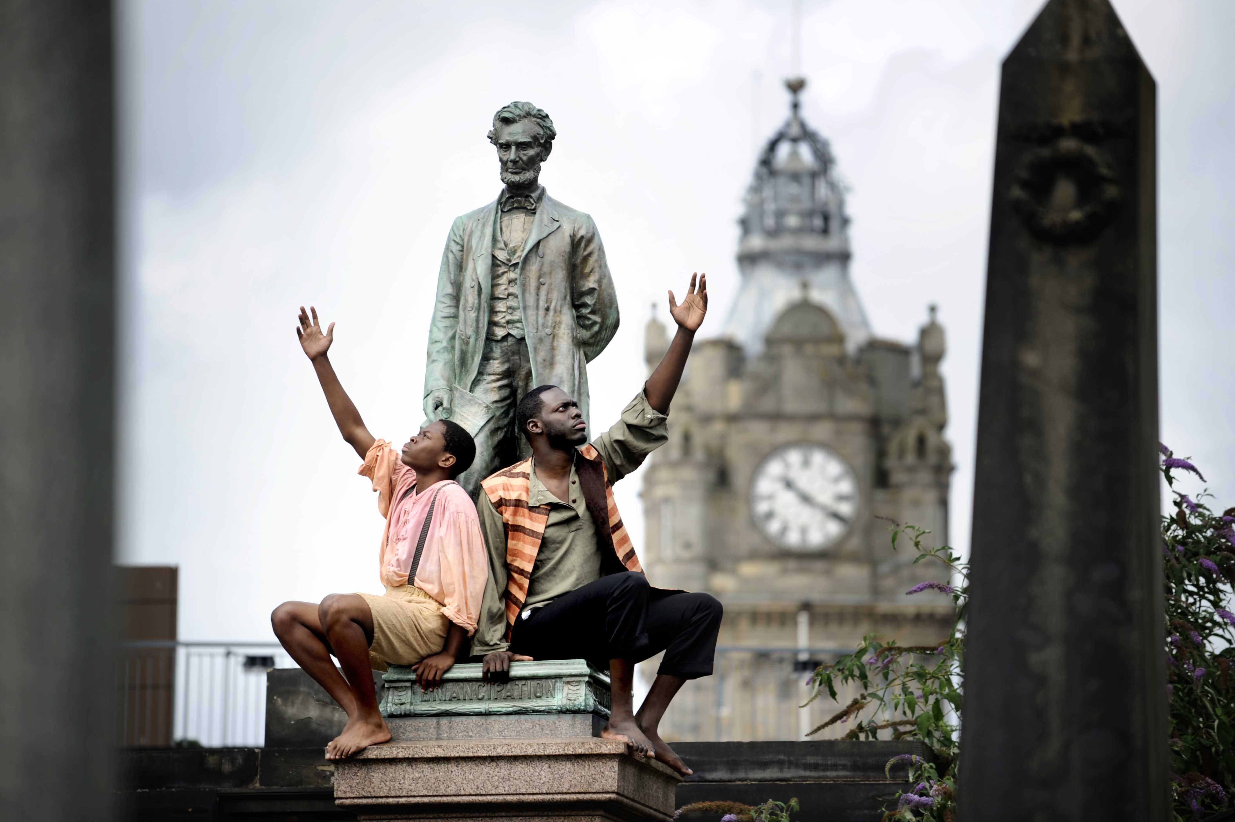 In Edinburgh, Scotland, two cast members of Henry Box Brown pose in front of a statue of Abraham Lincoln, the United States president who abolished slavery.