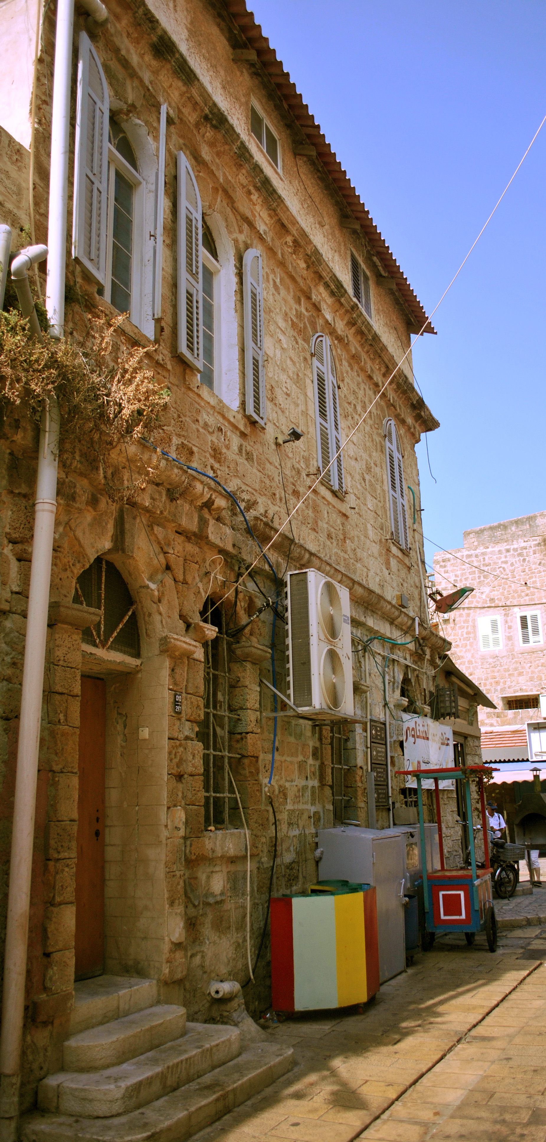 The building of the police station, where Bahá’u’lláh was first taken to be held in Akka on 31 August 1868, is now a coffee shop. The original structure was two stories. Two additional features can be seen in this photo: a third floor on top and a one-story extension at the end of the building.