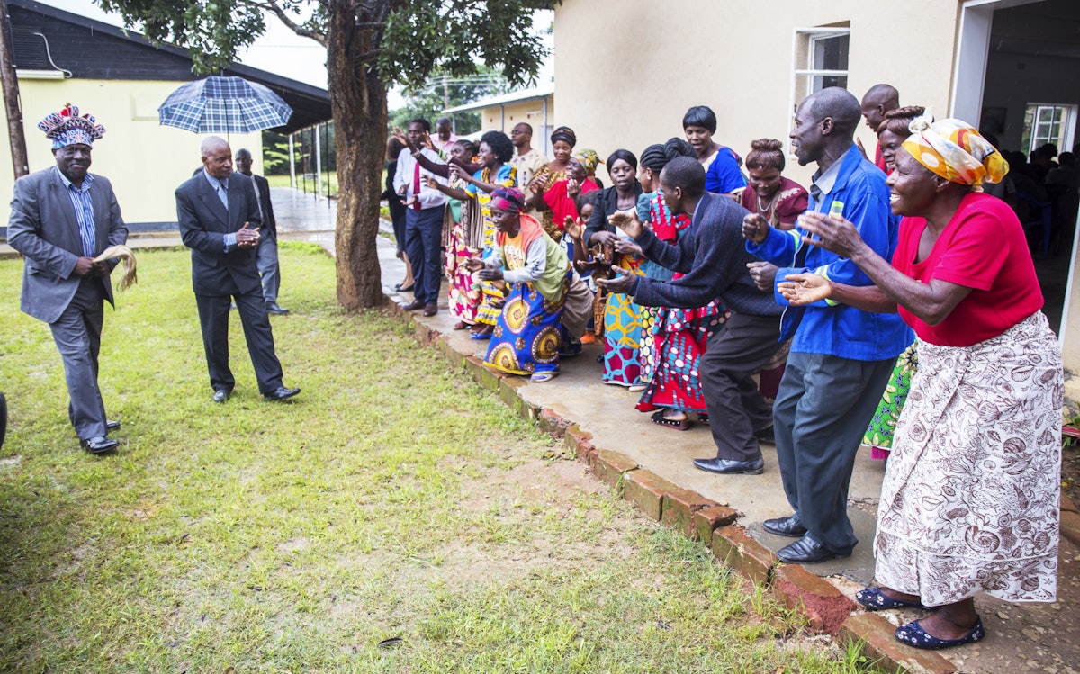 شرکت کنندگان در مراسم افتتاحیۀ ساختمان‌های جدید مؤسسهٔ بهائی اریک منتون در موینیلونگا، زامبیا در حال خوش‌آمدگویی به رئیس قبیله کانونگشا (سمت چپ).
