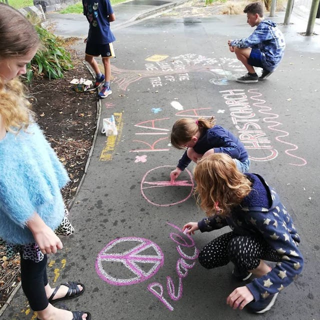 A group of young people draw chalk art on a sidewalk in Christchurch. A group of families involved in Baha’i community building activities in a neighborhood began the street art activity to inspire hope following the 15 March terror attacks.