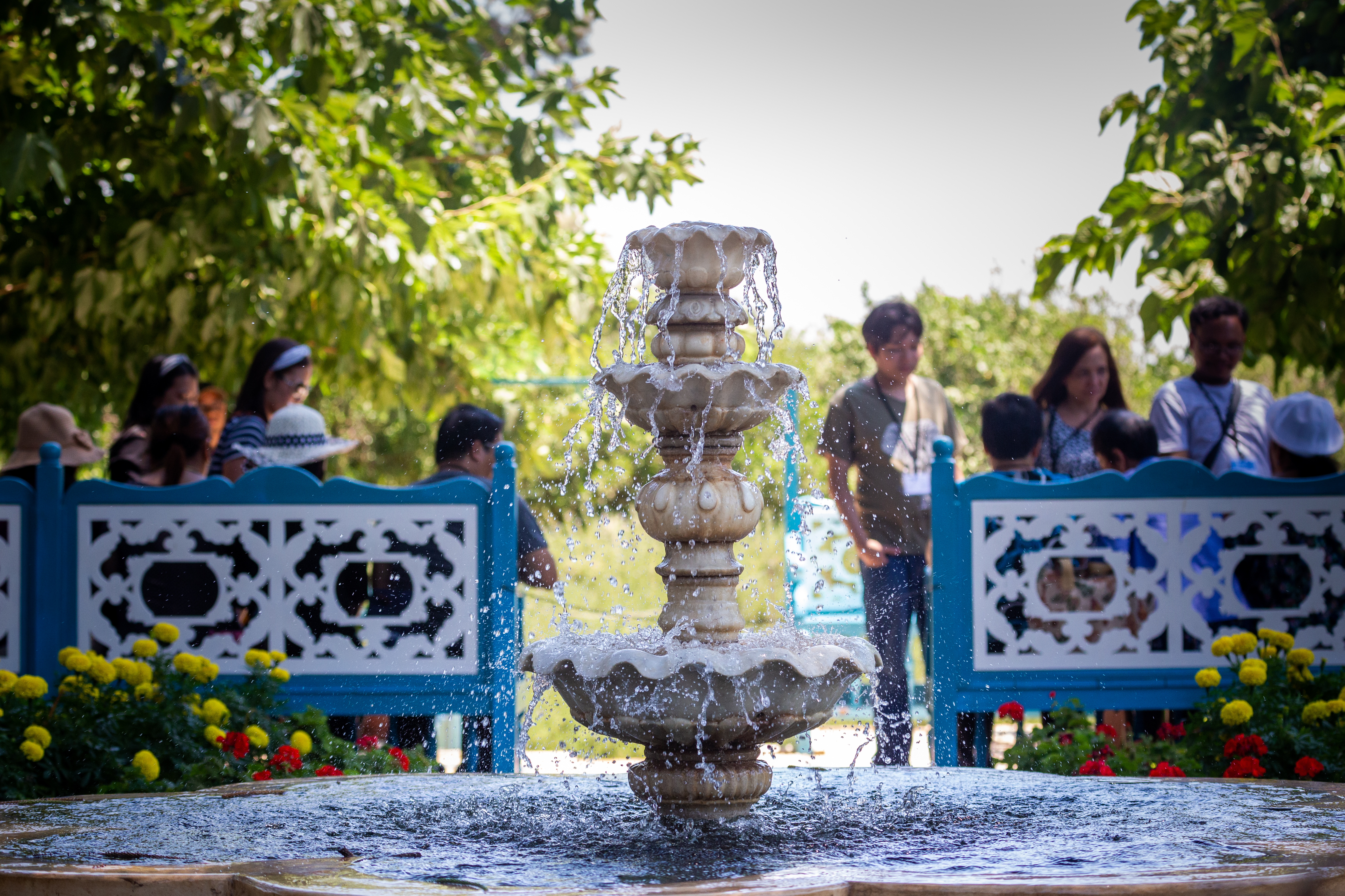 زائران پشت فواره‌ای قدیمی، روی نیمکت‌ها می‌نشینند و از باغ‌‌ها لذت می‌برند.