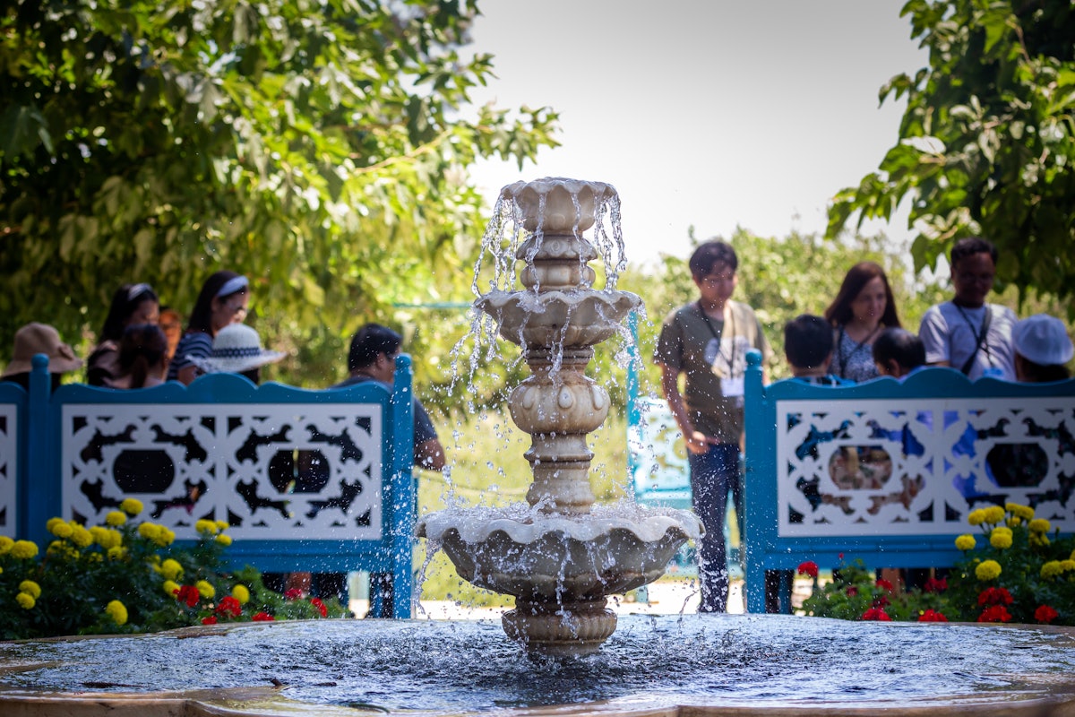 Pilgrims sit on the benches and enjoy the gardens with a historic fountain behind them.