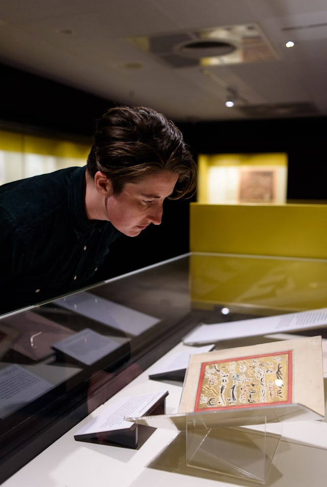 یکی از بازدیدکنندگان کتابخانهٔ بریتانیا در حال تماشای نسخهٔ اصل متون بهائی که به عنوان بخشی از نمایشگاه متون مقدس ادیان مختلف به نمایش در آمده. (عکس از ریچارد ایتون، هیئت‌مدیرهٔ کتابخانهٔ بریتانیا)