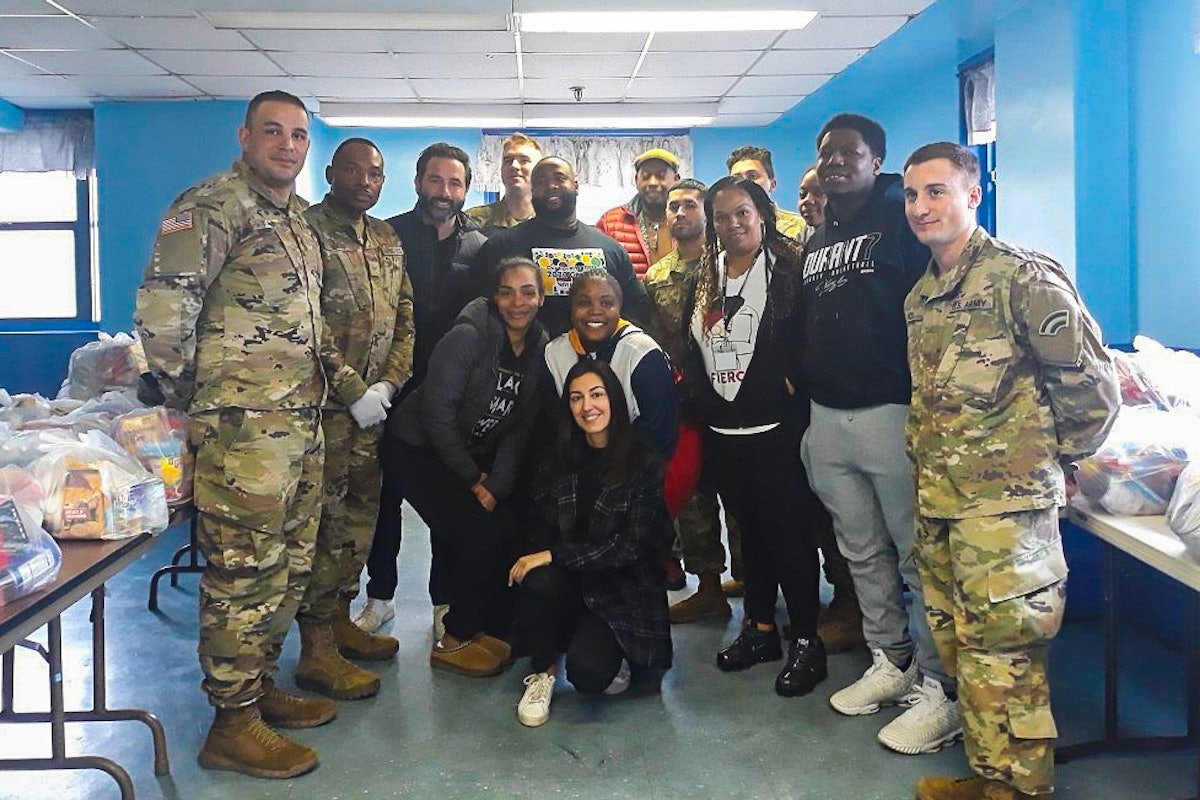 Esta fotografía muestra a los jóvenes y a los miembros de la Guardia Nacional antes de que entraran en vigor las precauciones sanitarias adicionales relacionadas con el distanciamiento. Los dispositivos de distribución de alimentos puestos en marcha por los jóvenes en New Rochelle, Nueva York, después del cierre de las escuelas de la zona, pronto fueron adoptados como punto oficial de distribución de alimentos por la Guardia Nacional del Estado.