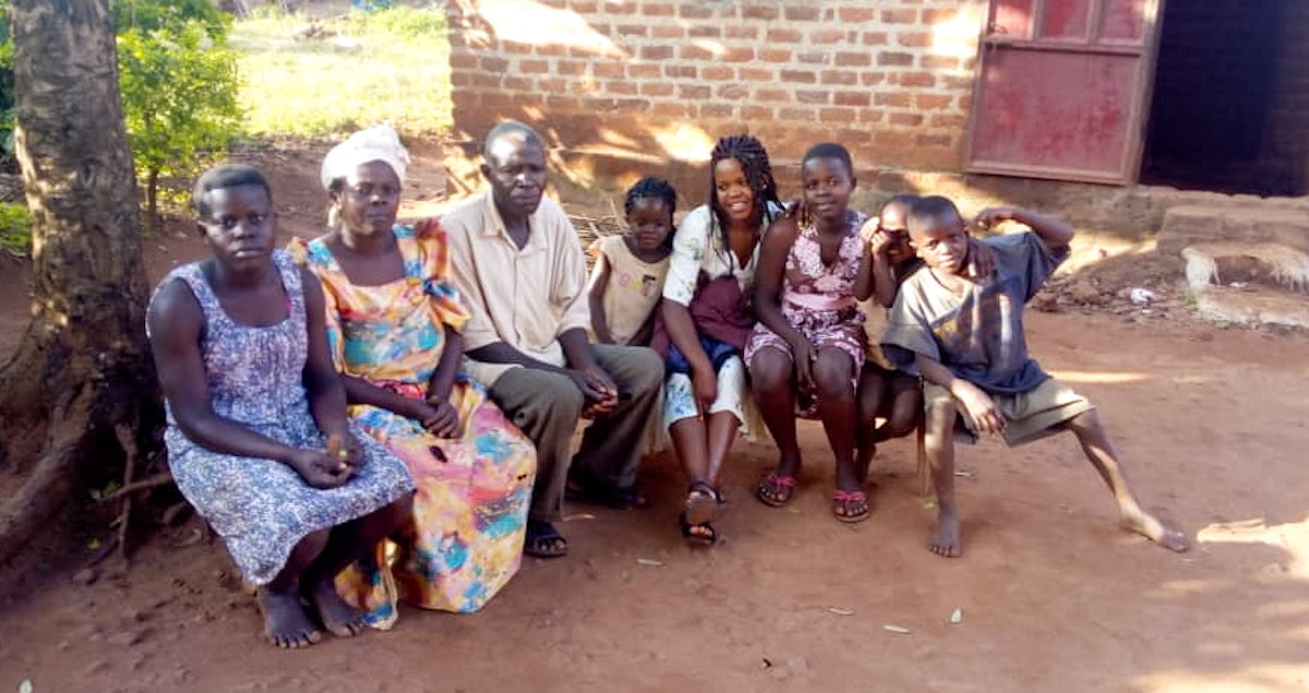 Image features residents of the same household. A family gathered outside their home in Kiyunga, Uganda, listen to a broadcast presented by the Baha’is of the village. Although public gatherings, including those for worship, are suspended across the country, residents of the same home are encouraged to continue praying among themselves.