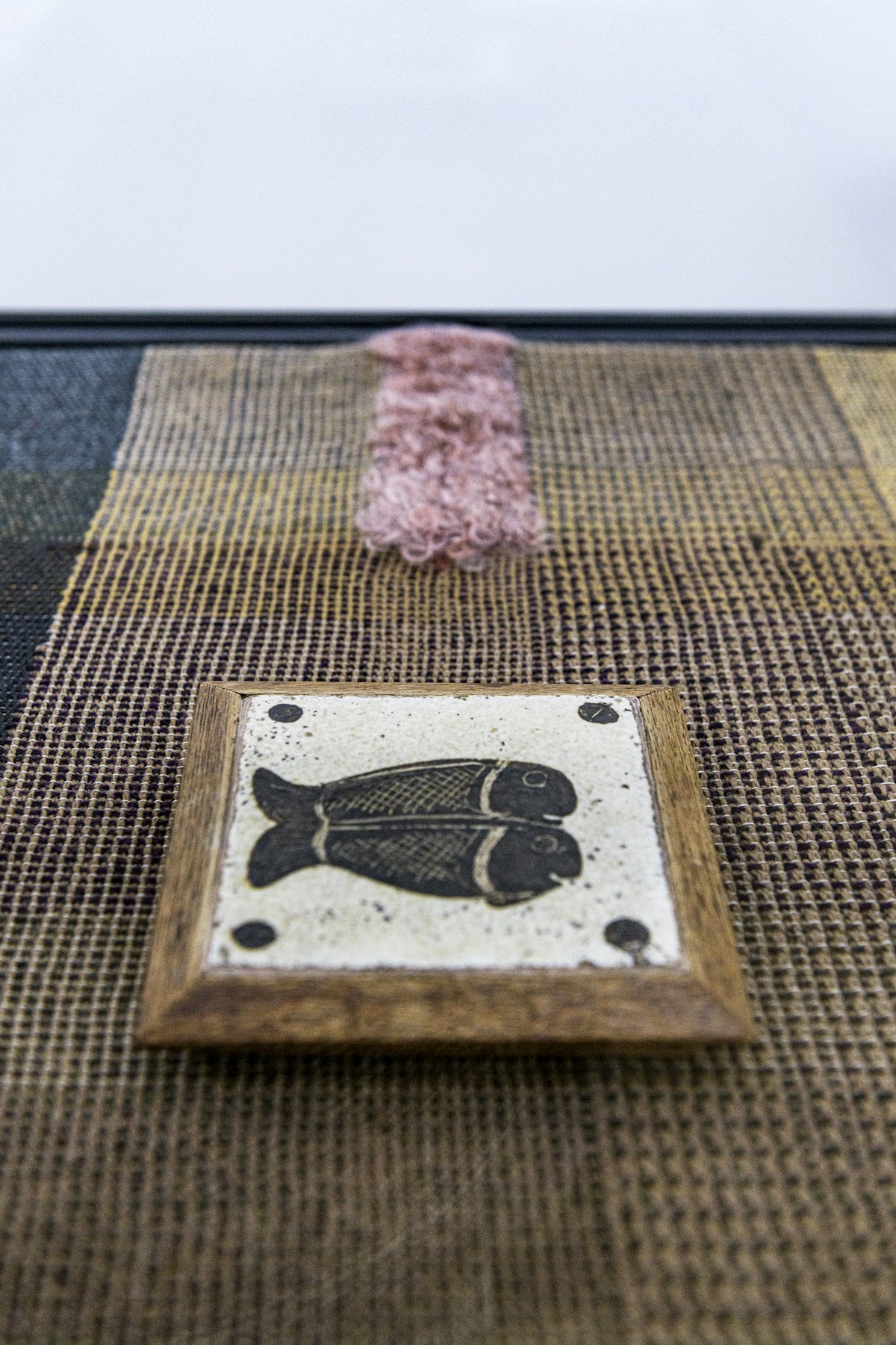 Un carreau décoré de poissons de Bernard Leach exposé sur un tissu tissé par l’artiste Travis Josef Meinolf, à l’installation de « Kai Althoff accompagne Bernard Leach » à la Galerie Whitechapel, Londres, 7 octobre 2020-10 janvier 2021. Photo : Polly Eltes
