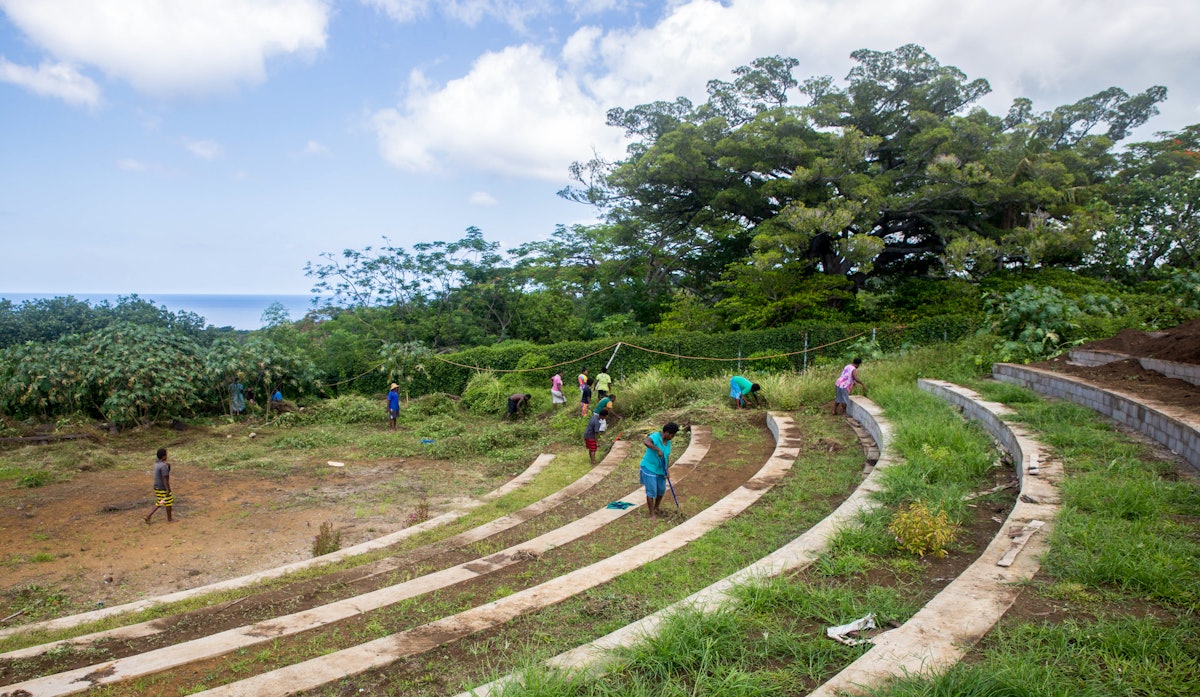 Miembros de la comunidad en torno al emplazamiento del templo ayudan a preparar un anfiteatro para las grandes reuniones de la comunidad en una ladera con bancales y con vistas al océano Pacífico.