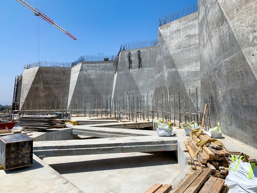 Un demi-cercle de murs plissés entoure désormais un côté de la place centrale. Le deuxième ensemble de murs plissés est en cours de construction, symétrique au premier sur le côté opposé de la place.