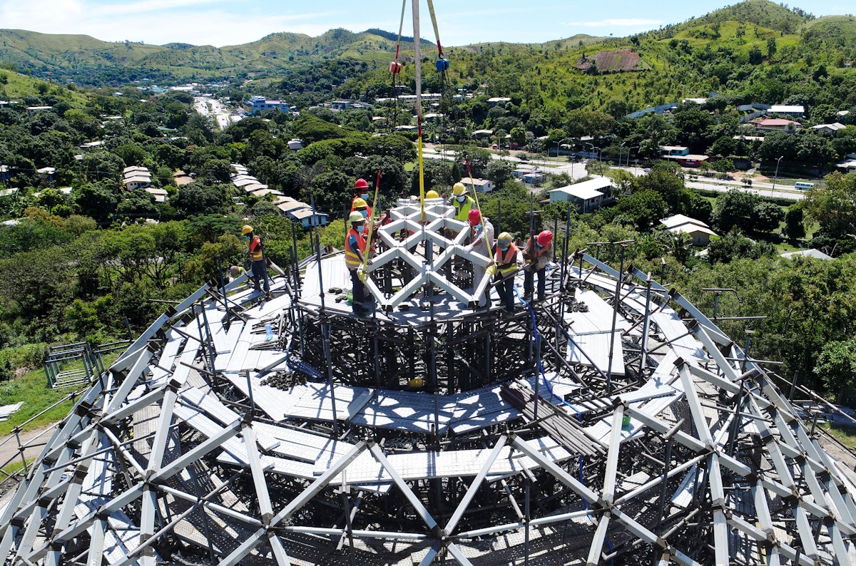 Construction workers raise the first of nine steel units of the dome into position.