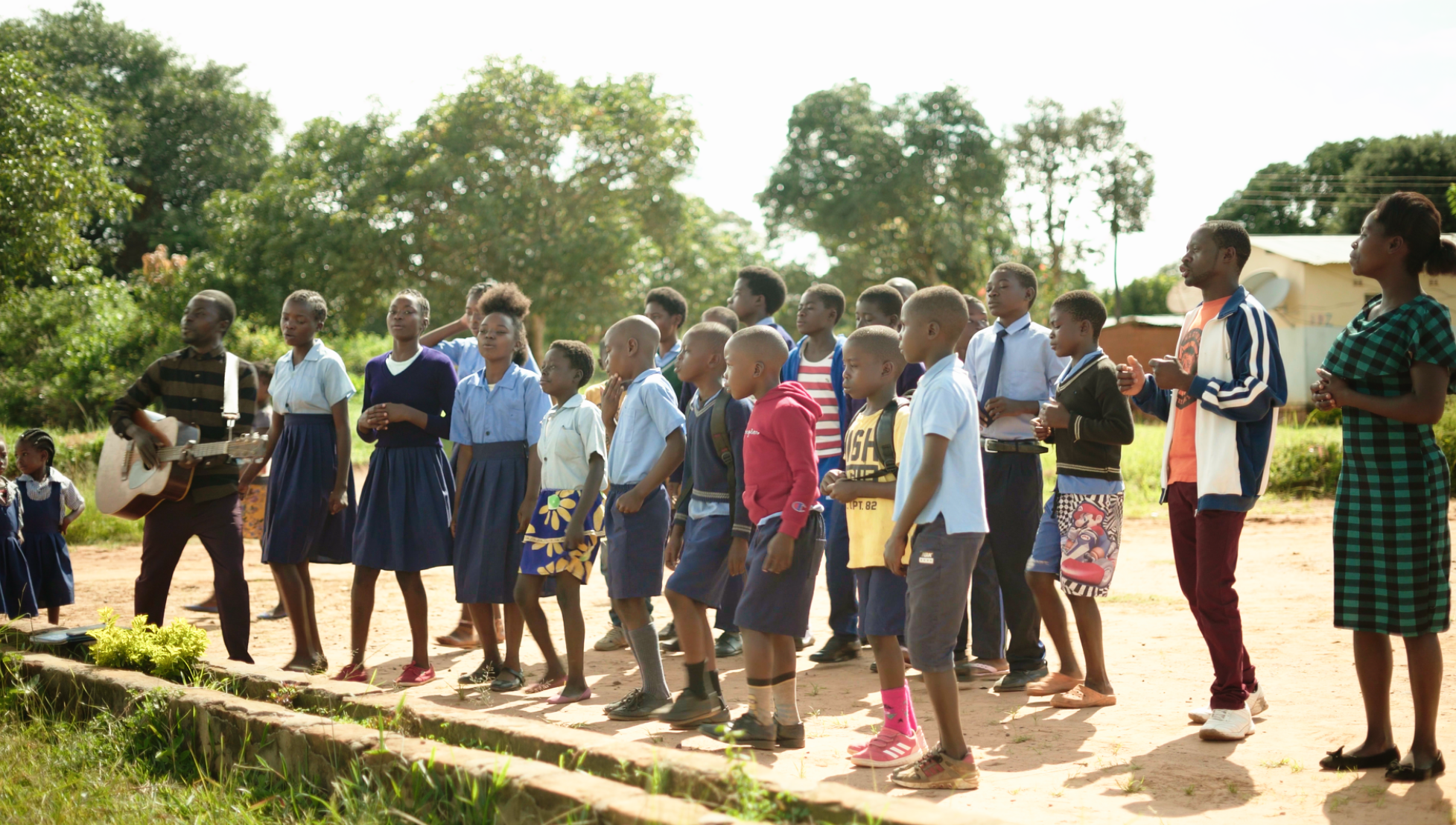 جوانان در حال خواندن سرودی در مورد ایجاد جوامع پویا، در جلسه‌ای در یک مدرسه در موینیلونگا (Mwinilunga).
