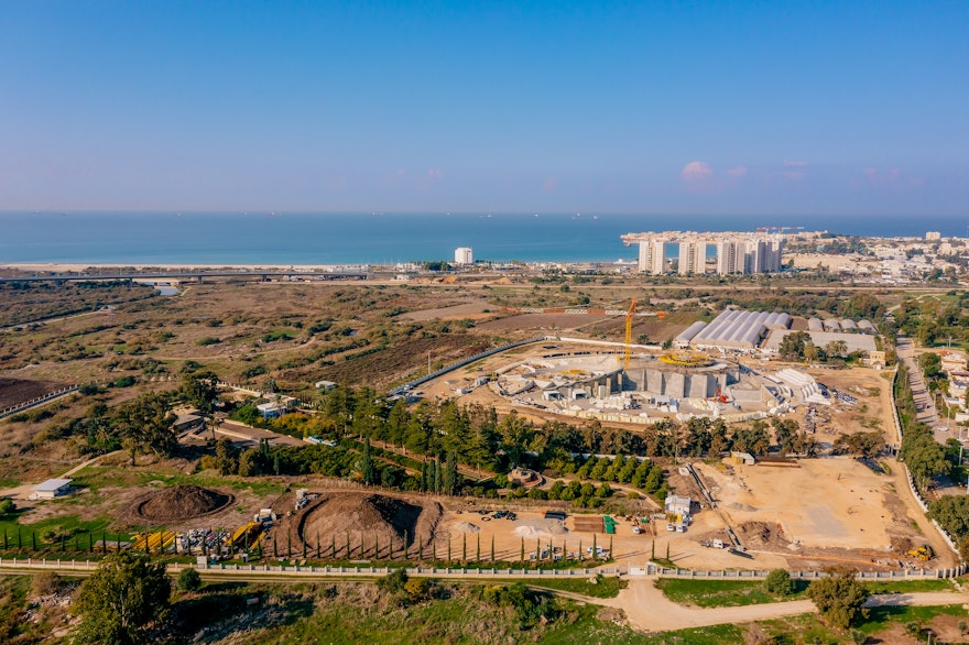 Alors que les travaux commencent sur les fondations du centre des visiteurs, la construction du sanctuaire lui-même continue à avancer rapidement. La vieille ville d’Acre est visible à arrière-plan, à droite.