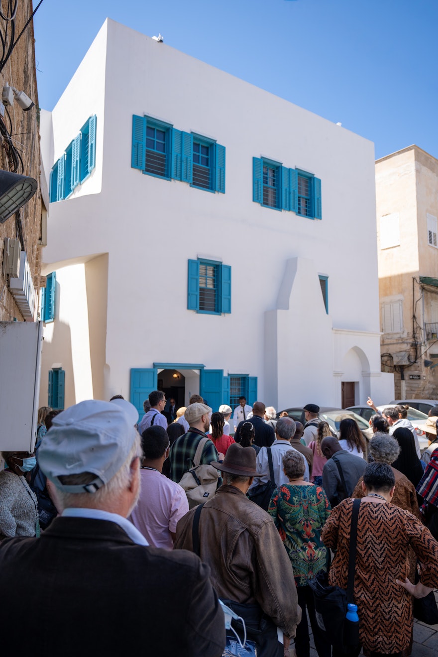 Delegates gather behind the House of ‘Abbúd before their visit. The upper-floor windows on the left seen above them are those of the room where Bahá’u’lláh revealed His Most Holy Book.