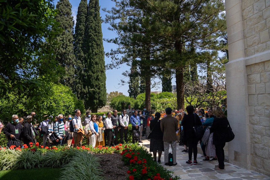 گروهی از شرکت‌کنندگان، از پیشینه‌های مختلف، به صحبت‌های راهنما در باغ‌های بیت حضرت عبدالبهاء، گوش فرا می‌دهند.