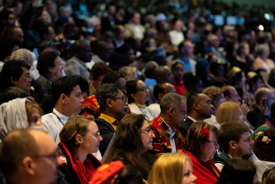 Convention participants listen intently, many receiving simultaneous translations as a delegate speaks.
