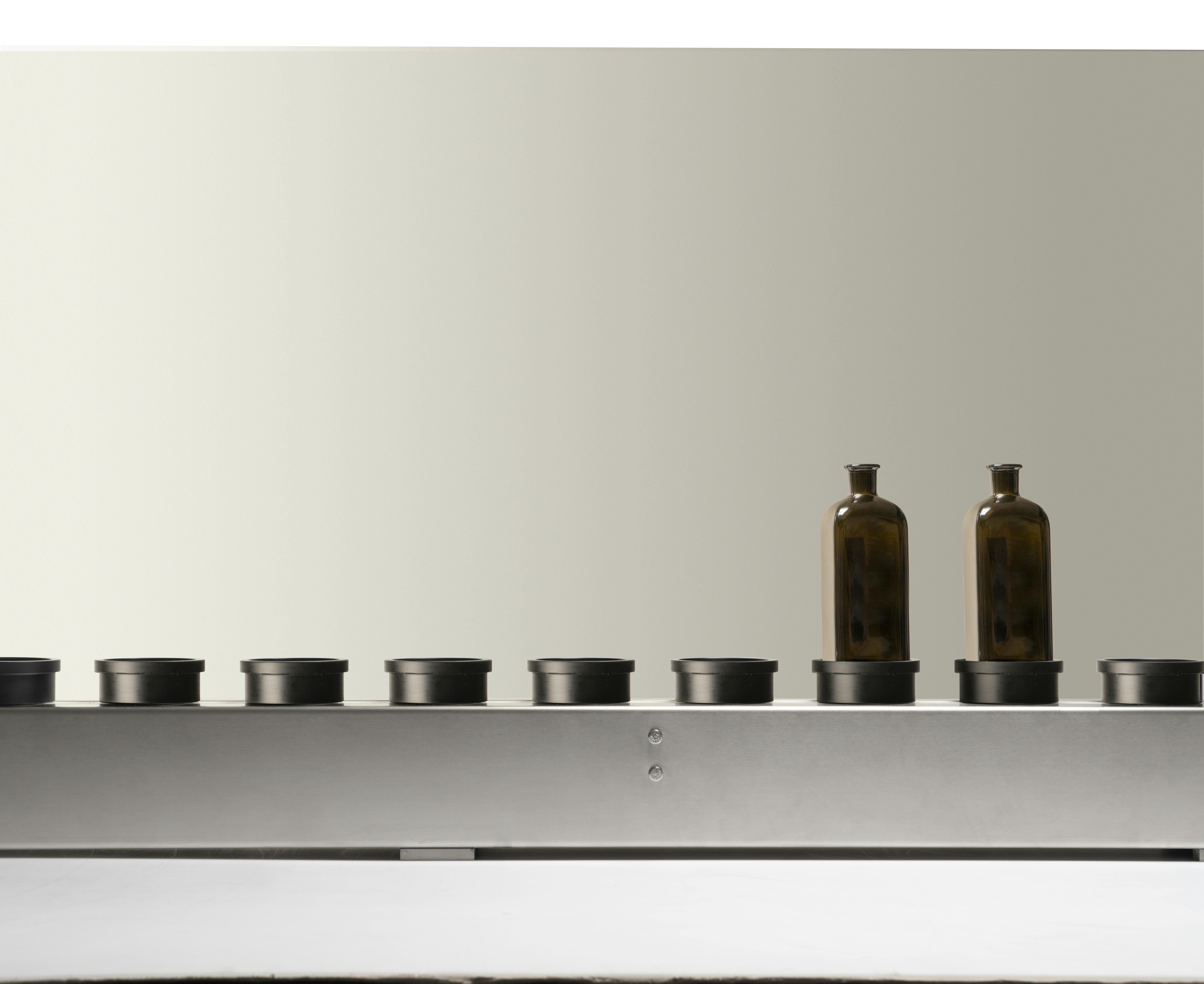 The conveyor belt present in Quinti machines, with two empty green glass bottles, suitable for spirits, on its plate