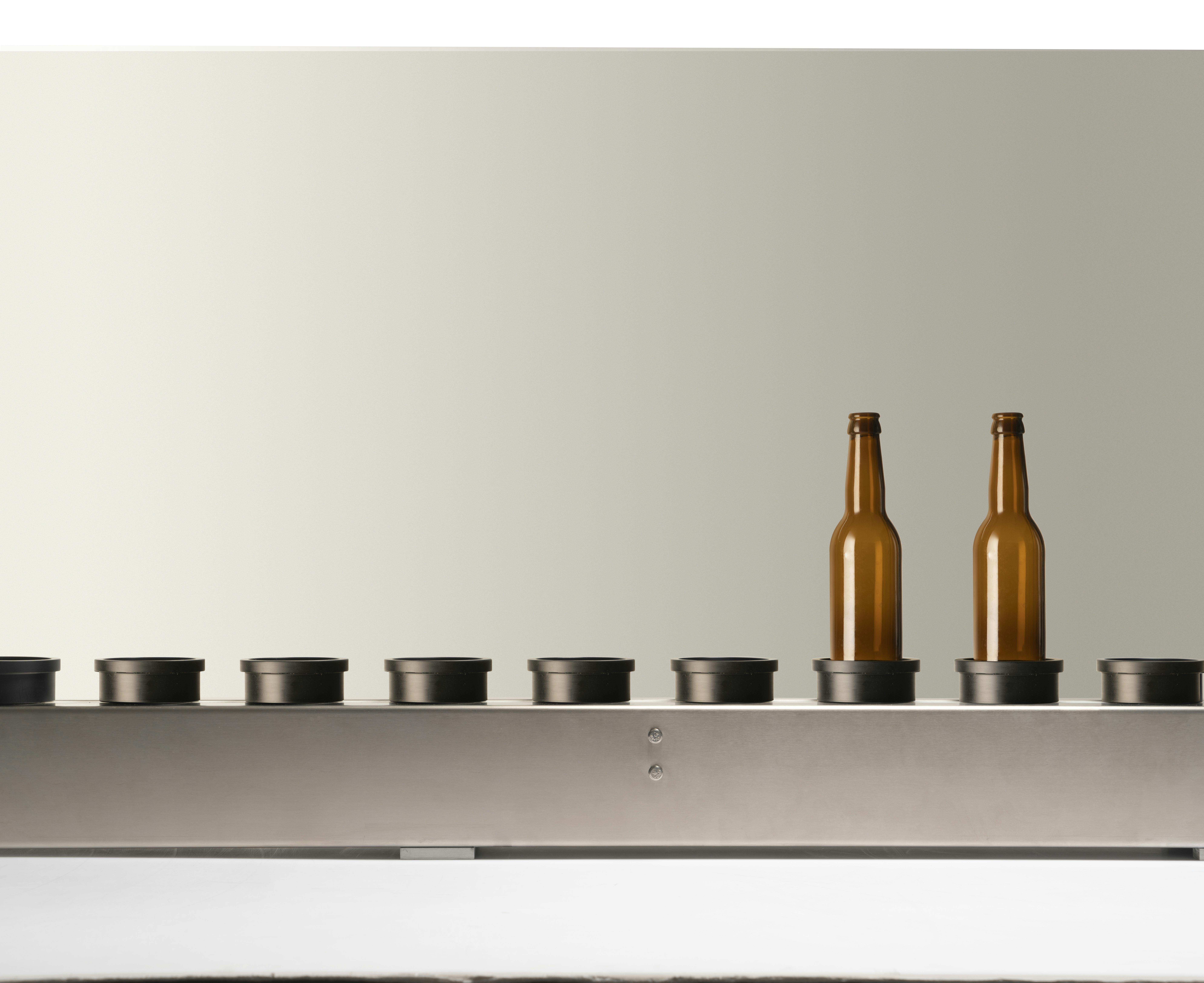 The conveyor belt present in Quinti machines, with two empty brown glass bottles, suitable for beer, on its plate