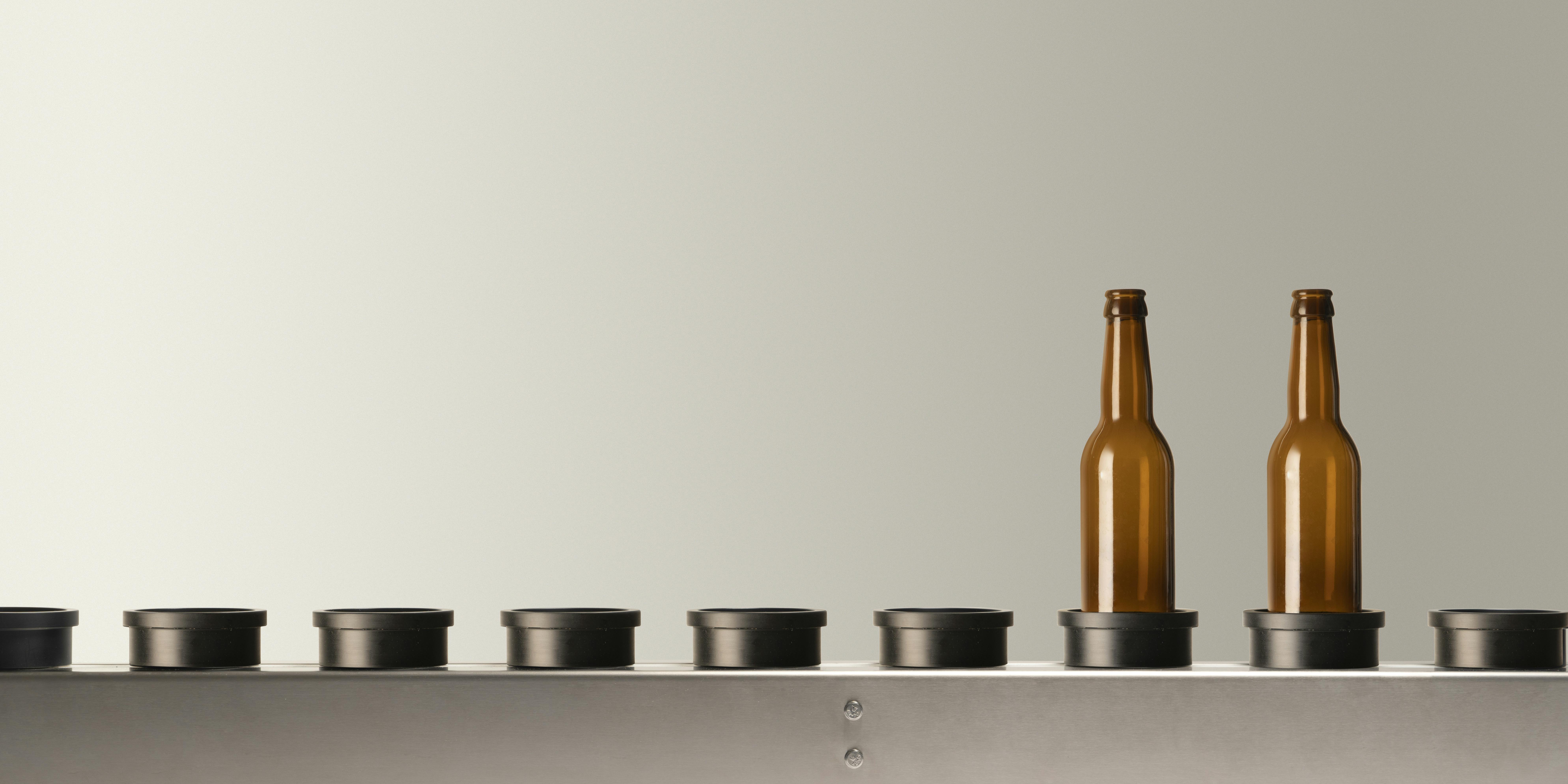 Il nastro trasportatore presente nelle macchine Quinti, con  due bottiglie di vetro vuote colore marrone, adatte per  birra, alloggiate sul proprio piattello