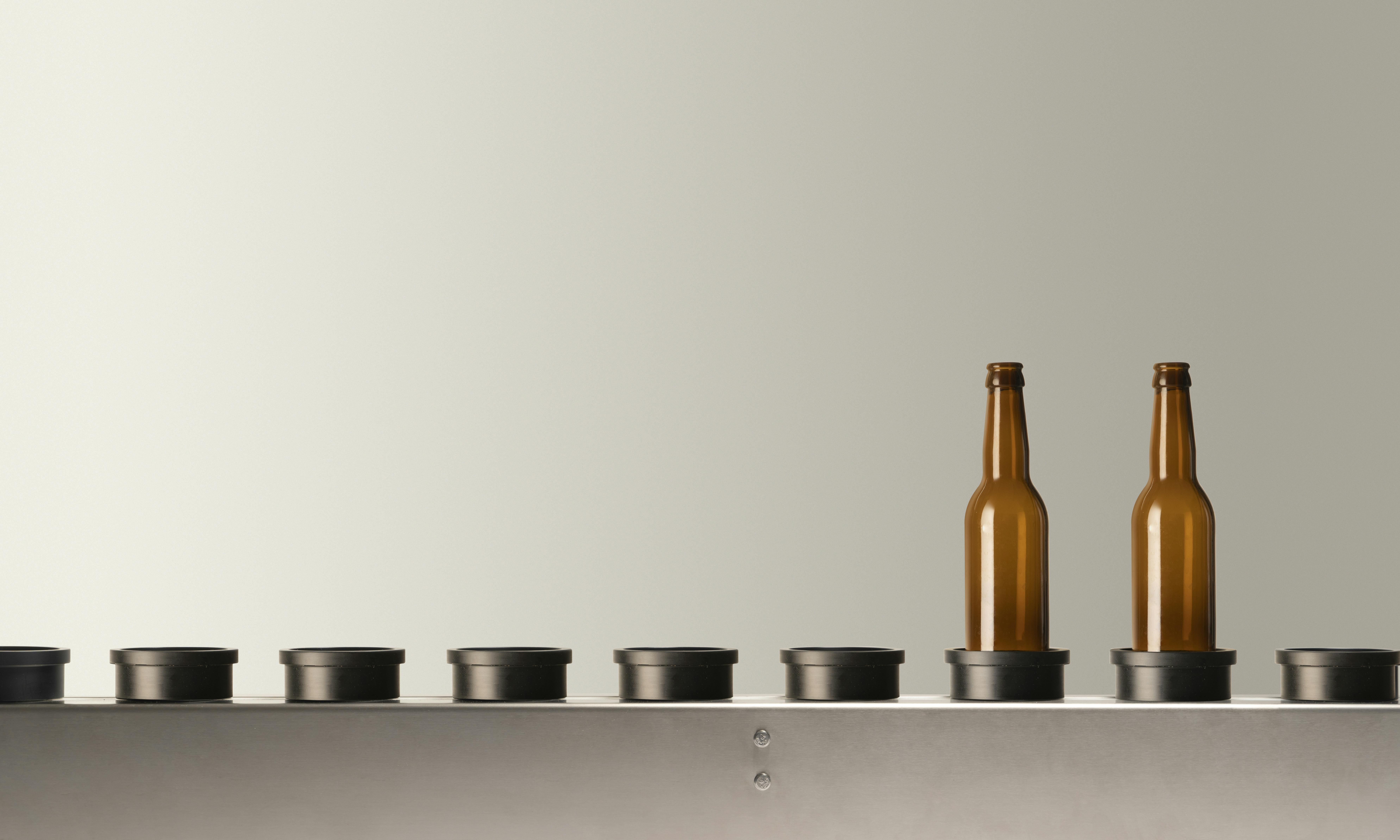 The conveyor belt present in Quinti machines, with two empty brown glass bottles, suitable for beer, on its plate