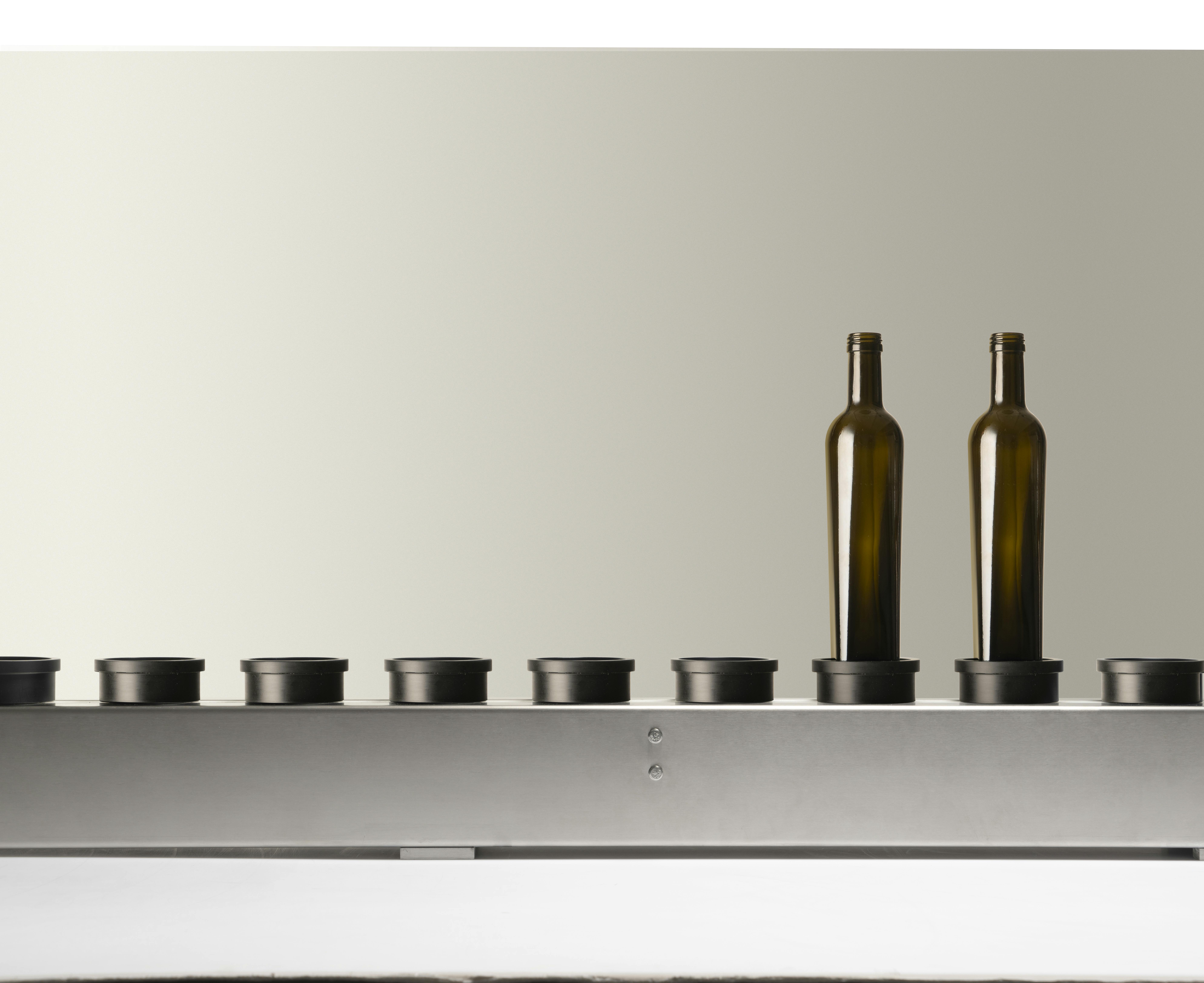 The conveyor belt present in Quinti machines, with two empty green glass bottles, suitable for oil, on its plate