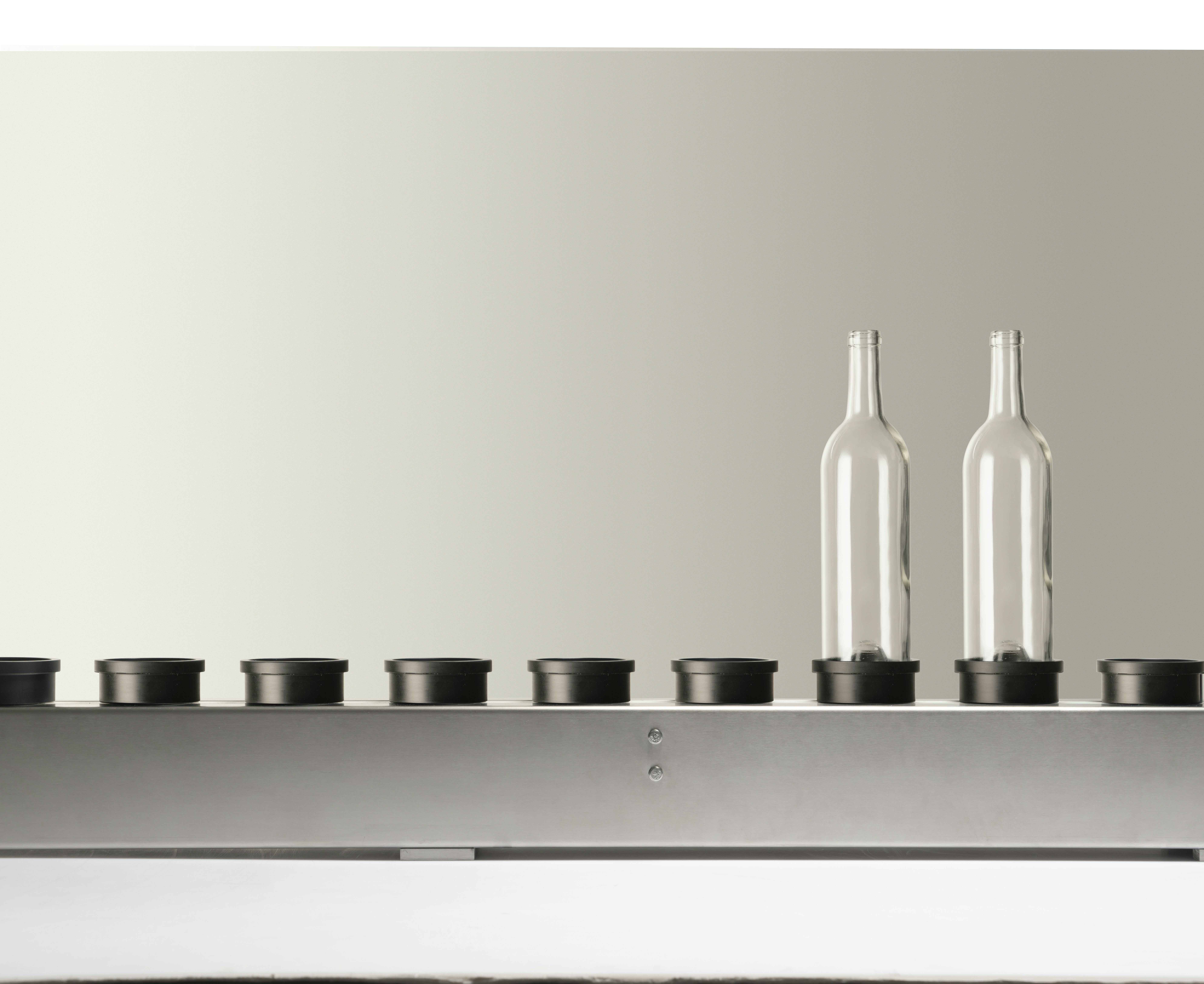 The conveyor belt present in Quinti machines, with two empty transparent glass bottles, suitable for wine, on its plate