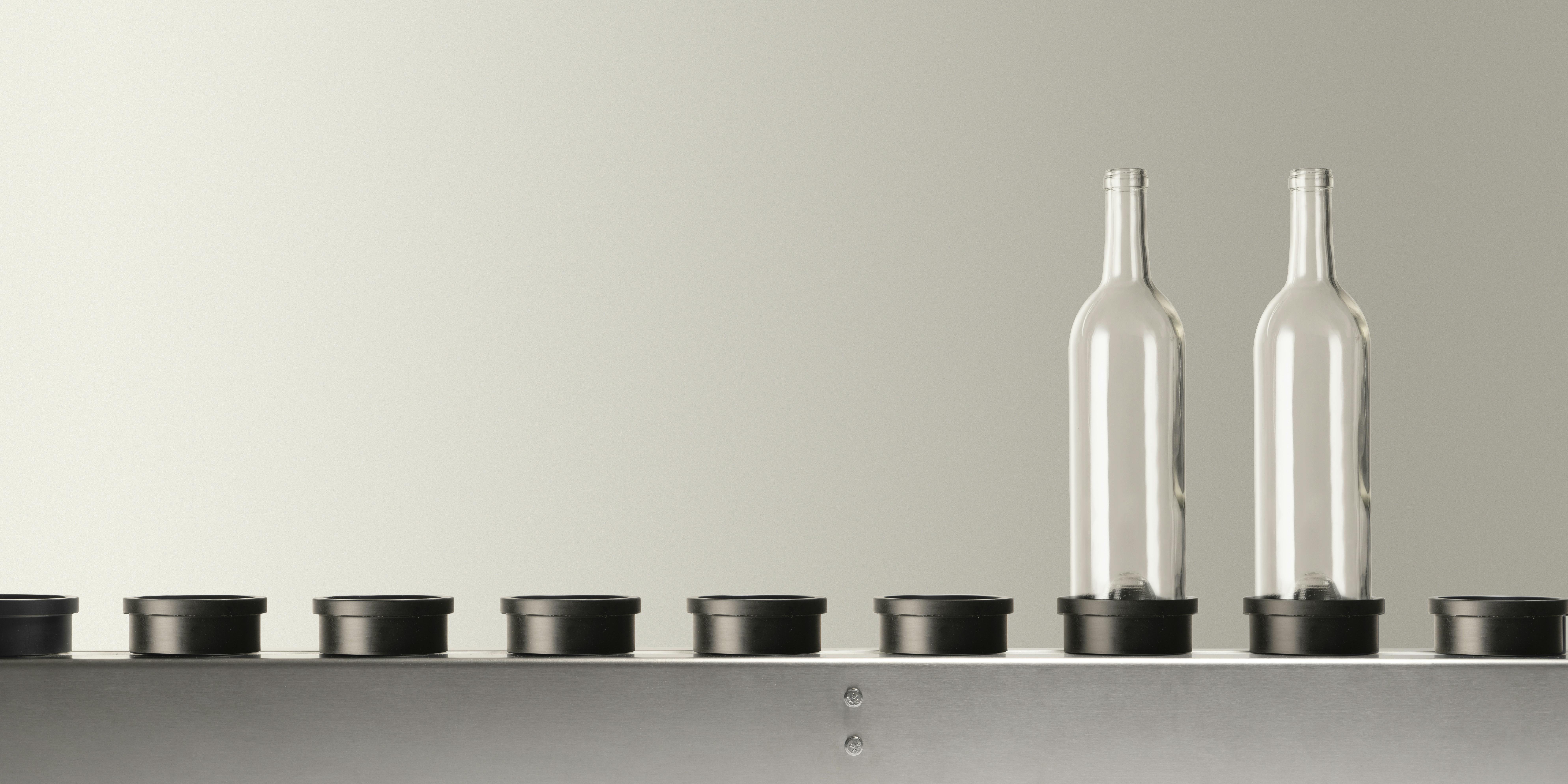 Il nastro trasportatore presente nelle macchine Quinti,  con  due bottiglie di vetro vuote colore trasparente, adatte per  vino, alloggiate sul proprio piattello