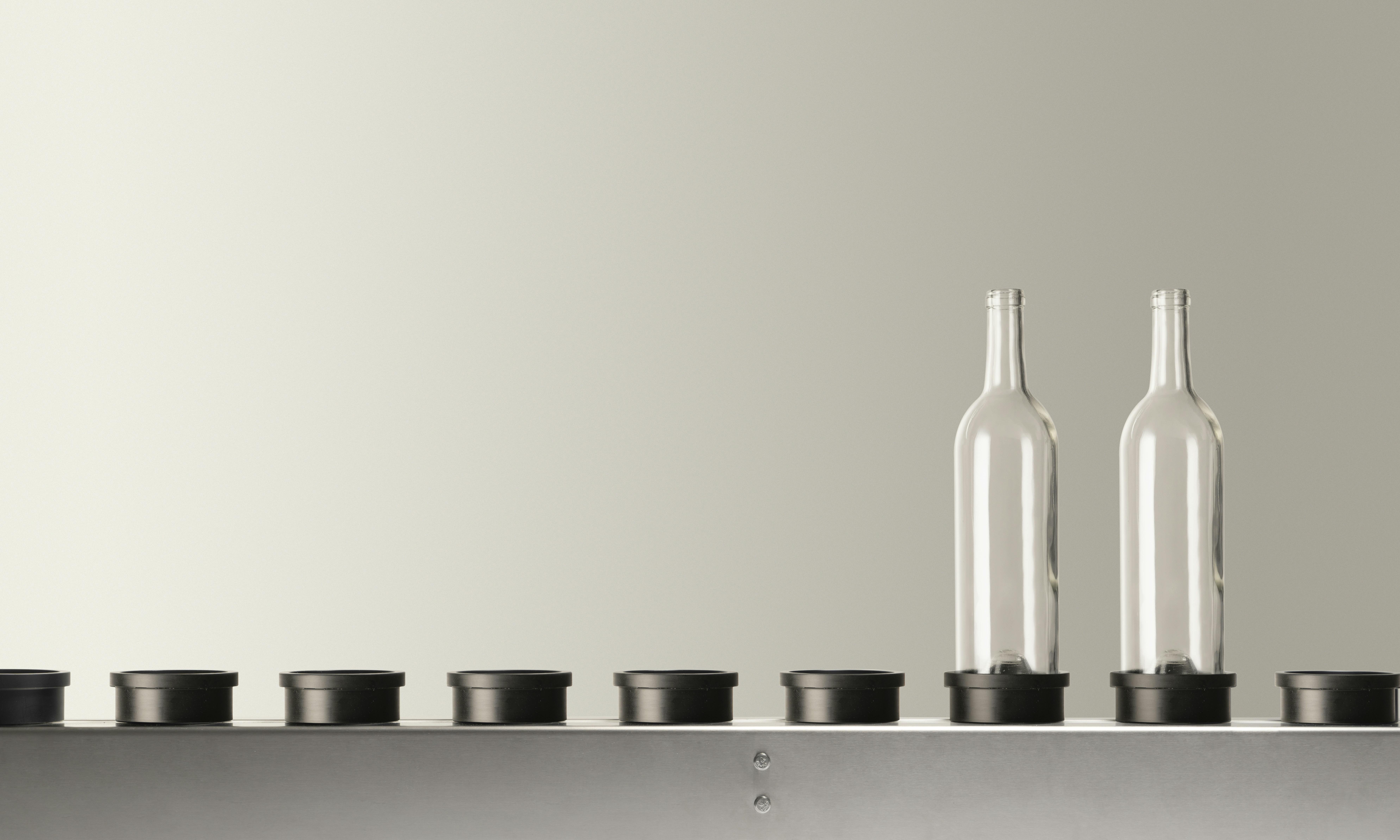 The conveyor belt present in Quinti machines, with two empty transparent glass bottles, suitable for wine, on its plate